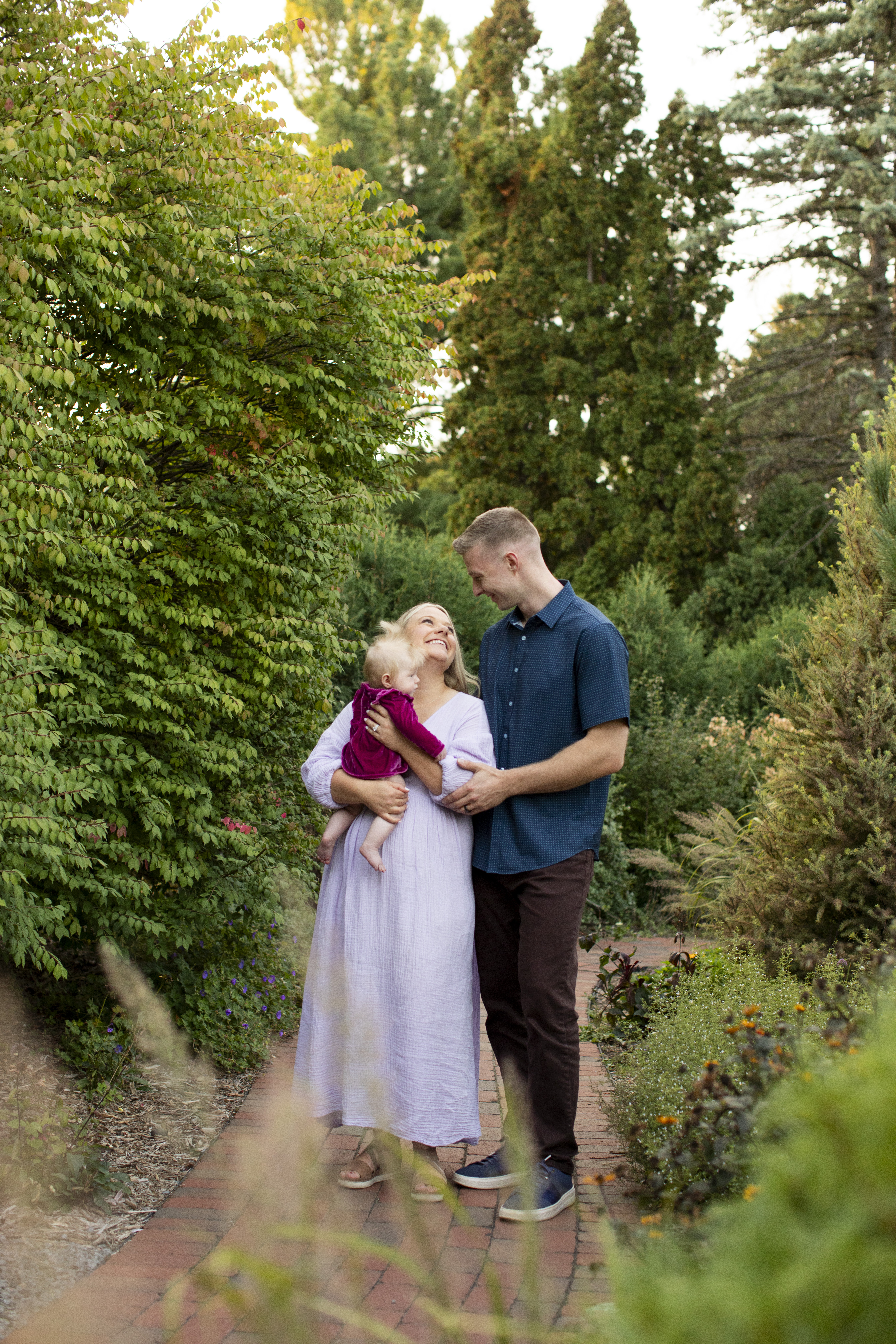 Danielle Rose Nelson with her husband and daughter in a garden setting at a fountain